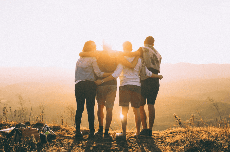 four friends standing on a hill at sunset holding each other