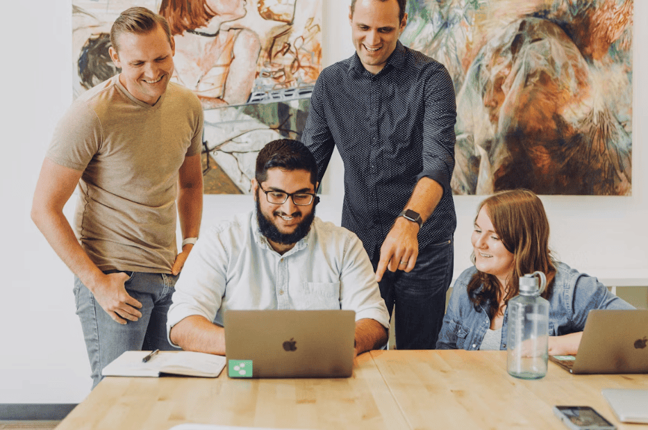 group at work talking and one man sat at a laptop with others around him