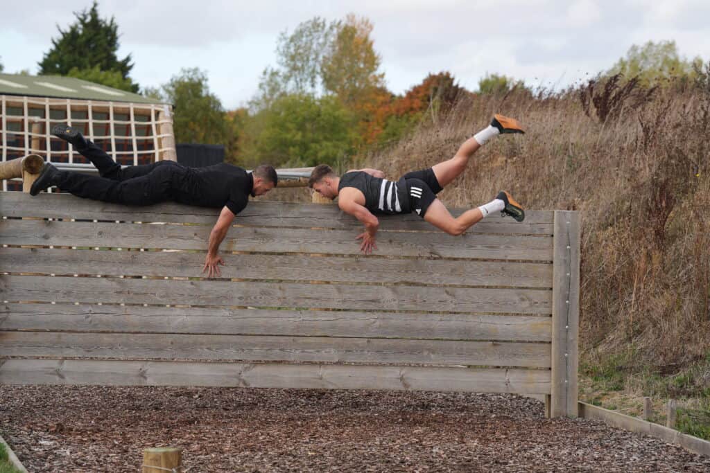Two men climbing an assault course wall.
