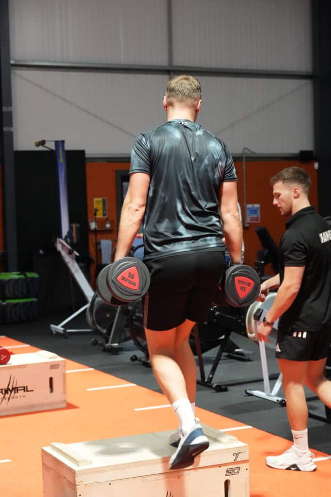 A gym member holding weights with a personal trainer